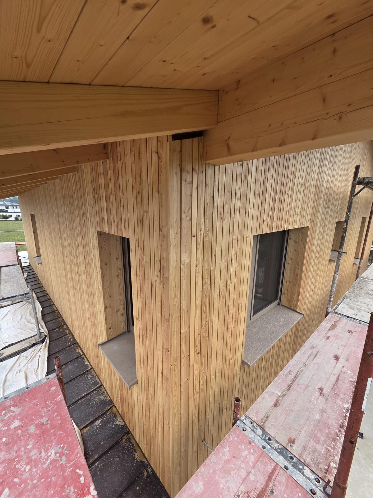 Neue vertikale Holzfassade mit Fenstern unter dem Dachüberstand